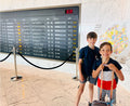 Two children standing in front of an airport departure board with a map in the background.